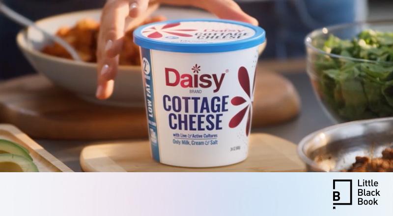 Daisy Cottage Cheese being placed on kitchen table.Little Black Book logo
